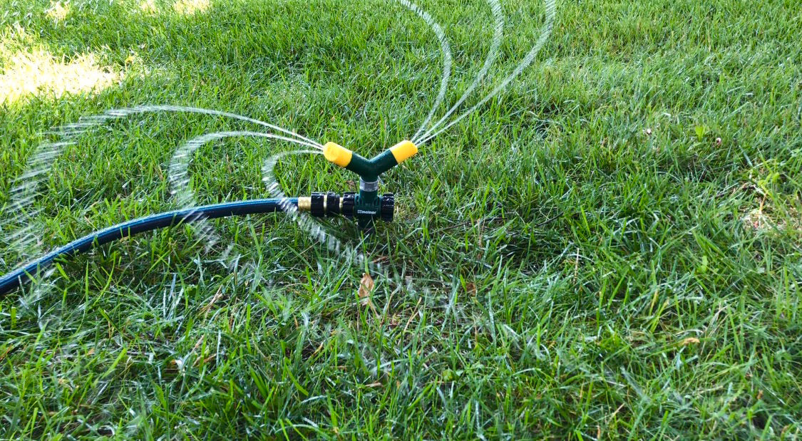 Green and yellow Melnor two arm revolving sprinkler model number 9575C sprays water on a green lawn.