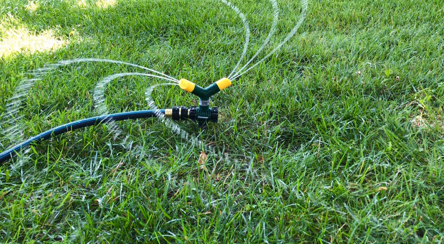 Green and yellow Melnor two arm revolving sprinkler model number 9575C sprays water on a green lawn.