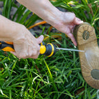 A person outdoors uses the Melnor R901 Mini Nozzle to rinse a brown sole of a shoe over green grass.