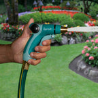 A person's hand is holding a green and black garden hose nozzle named "Sprout," spraying water, with a vibrant, colorful flowerbed and greenery in the background.