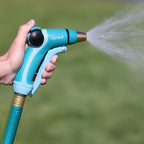 A person's hand is holding a blue and green garden hose nozzle, labeled "Sprout," spraying a mist of water against a blurred green grass background.