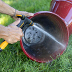 Melnor XT300 Front Trigger Metal Adjustable Nozzle with Flow Control using the targeted jet spray setting on a large red plastic planting pot on green grass.