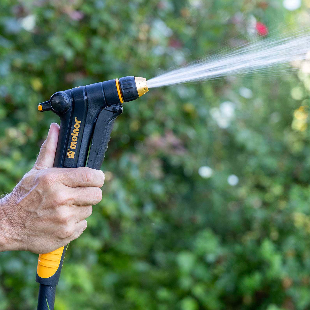 Melnor XT300 Front-Trigger Adjustable Nozzle with Flow Control turned to the jet setting in front of a blurred garden background.