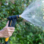 Melnor XT300 Front-Trigger Adjustable Nozzle with Flow Control turned to the mist setting in front of a blurred garden background.