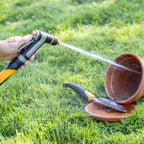 Person using Melnor XT450 Heavyweight Metal Adjustable Nozzle to water a terracotta pot on grass.