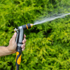 Person using the Melnor XT450 Heavyweight Metal Adjustable Nozzle in the Jet pattern to spray water on green foliage.