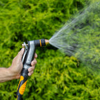 Person using the Melnor XT450 Heavyweight Metal Adjustable Nozzle in the Shower pattern to spray water on green foliage.