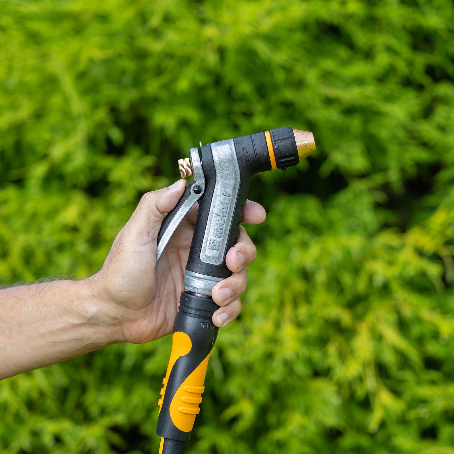 Hand holding the Melnor XT450 Heavyweight Metal Adjustable Nozzle against a green background.