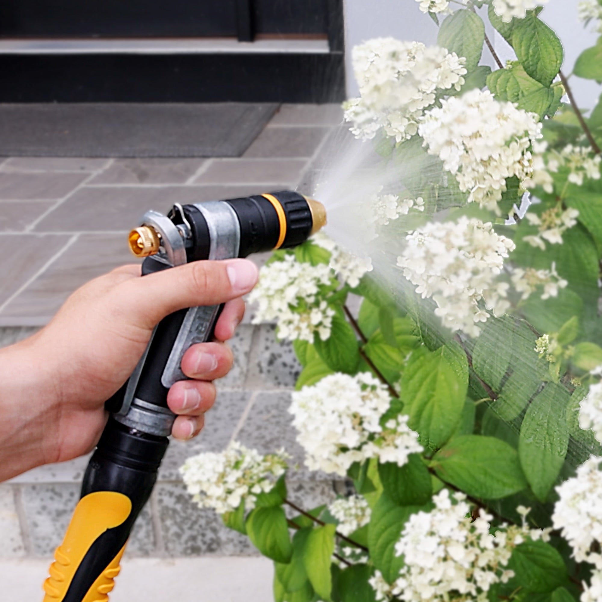 Person using the Melnor XT450 Heavyweight Metal Adjustable Nozzle to water white flowers.