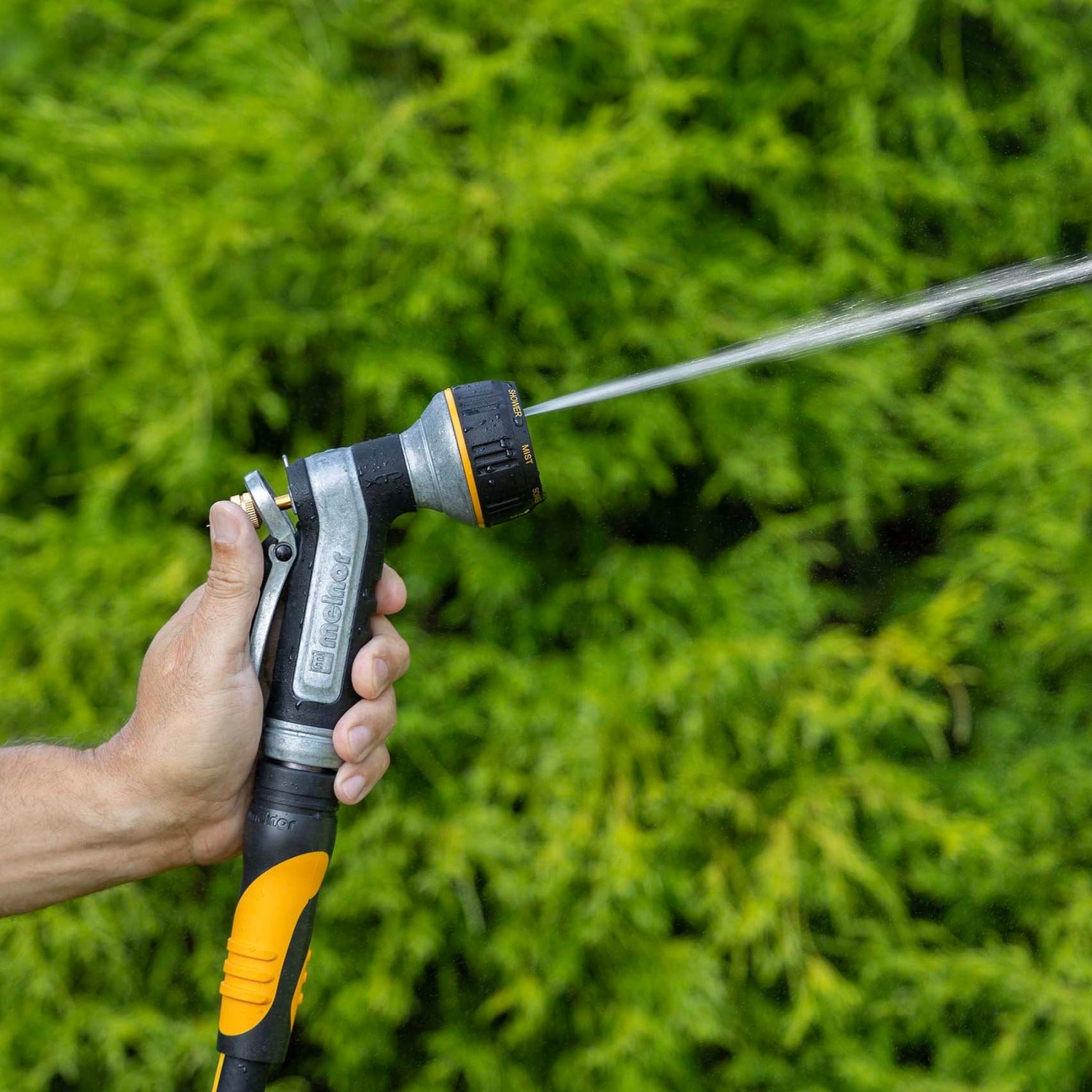 Hand holding the Melnor XT451 Heavyweight Metal 7-Pattern Nozzle in the Jet pattern against a green grass background.