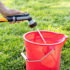 Person using the Melnor XT451 Heavyweight Metal 7-Pattern Nozzle in the Flat pattern to fill a red bucket on grass.