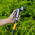 Hand holding the Melnor XT451 Heavyweight Metal 7-Pattern Nozzle against a green grass background.