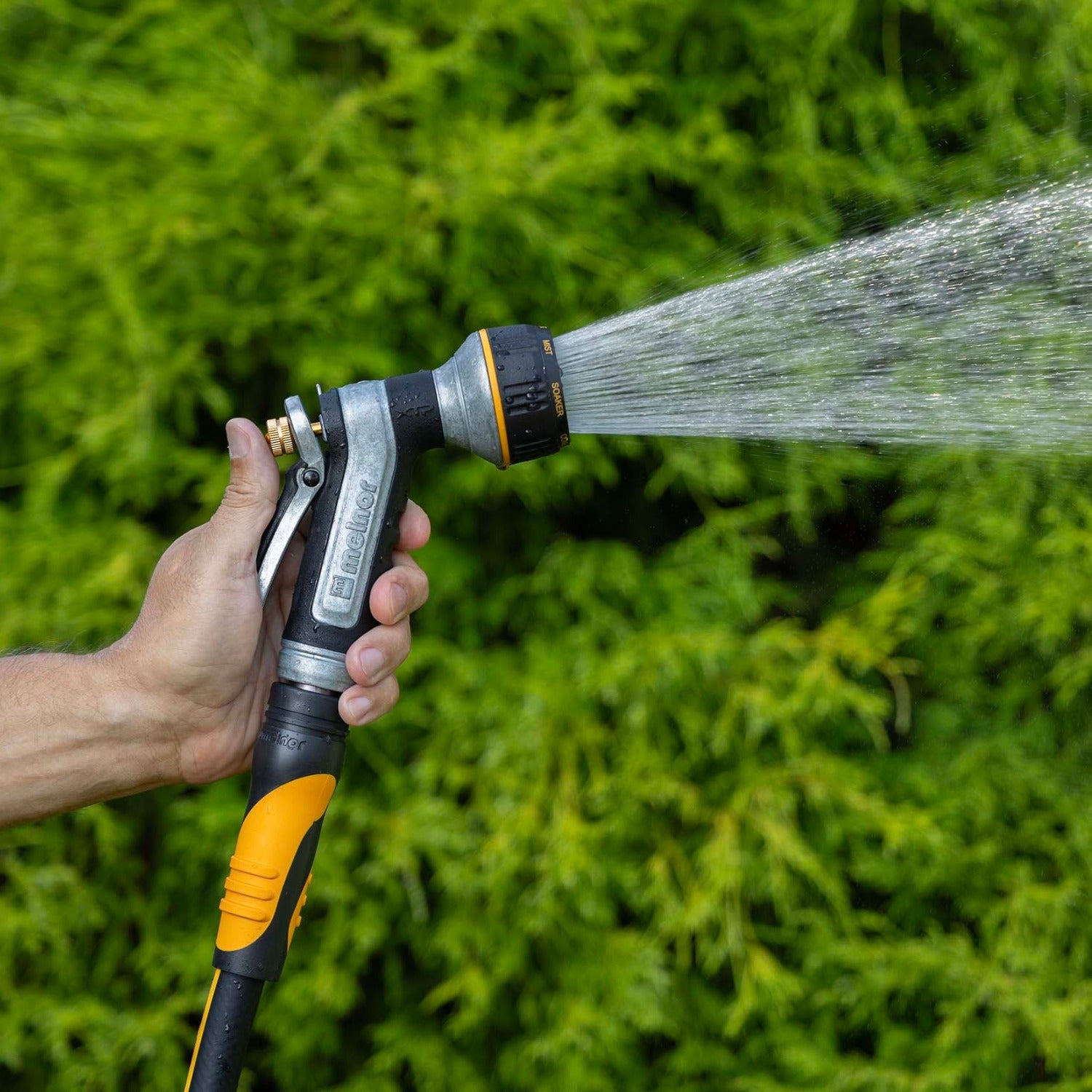 Hand holding the Melnor XT451 Heavyweight Metal 7-Pattern Nozzle in the Shower pattern against a green grass background.