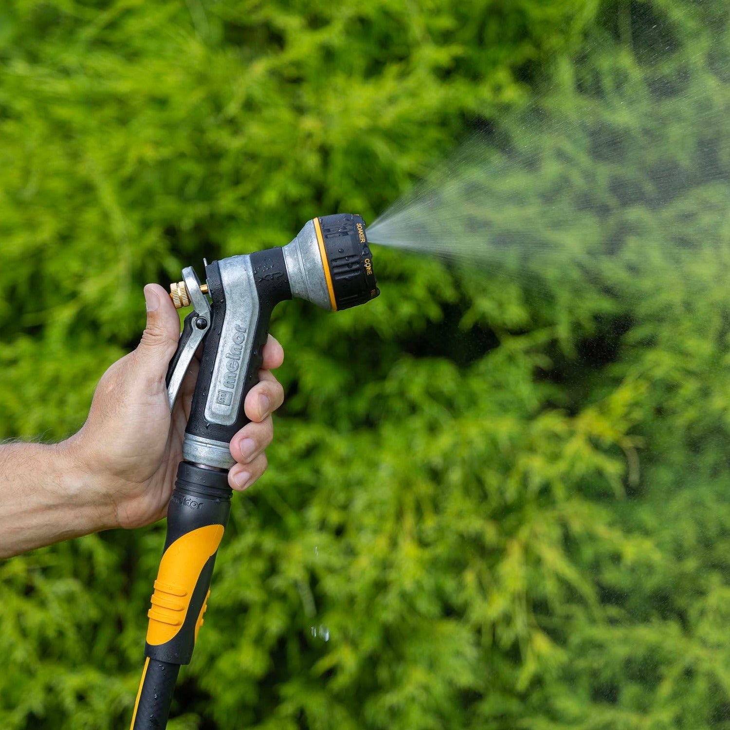 Hand holding the Melnor XT451 Heavyweight Metal 7-Pattern Nozzle in the Mist pattern against a green grass background.