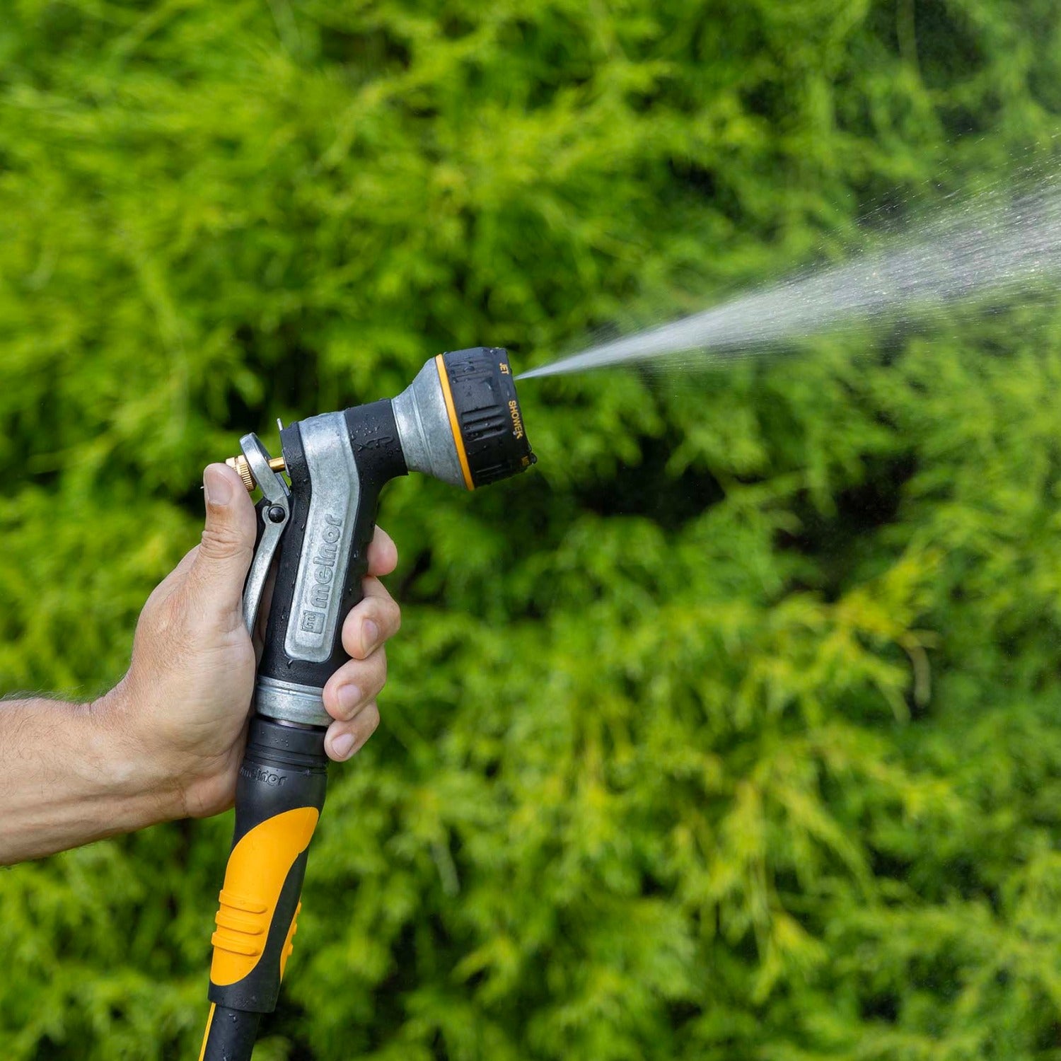 Hand holding the Melnor XT451 Heavyweight Metal 7-Pattern Nozzle in the Flat pattern against a green grass background.
