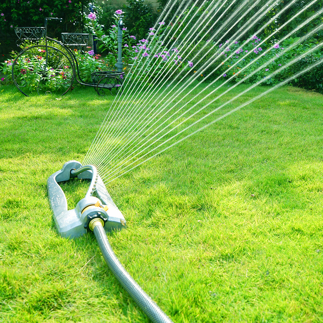 Melnor XT45360M garden sprinkler watering grass with a garden and flowers in the background.