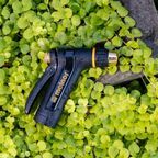 The Melnor XT200 Rear-Trigger Adjustable Nozzle laying on a bed of green clovers and a rock.