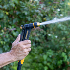 Melnor XT200 Rear-Trigger Adjustable Nozzle turned to the jet setting in front of a blurred garden background.