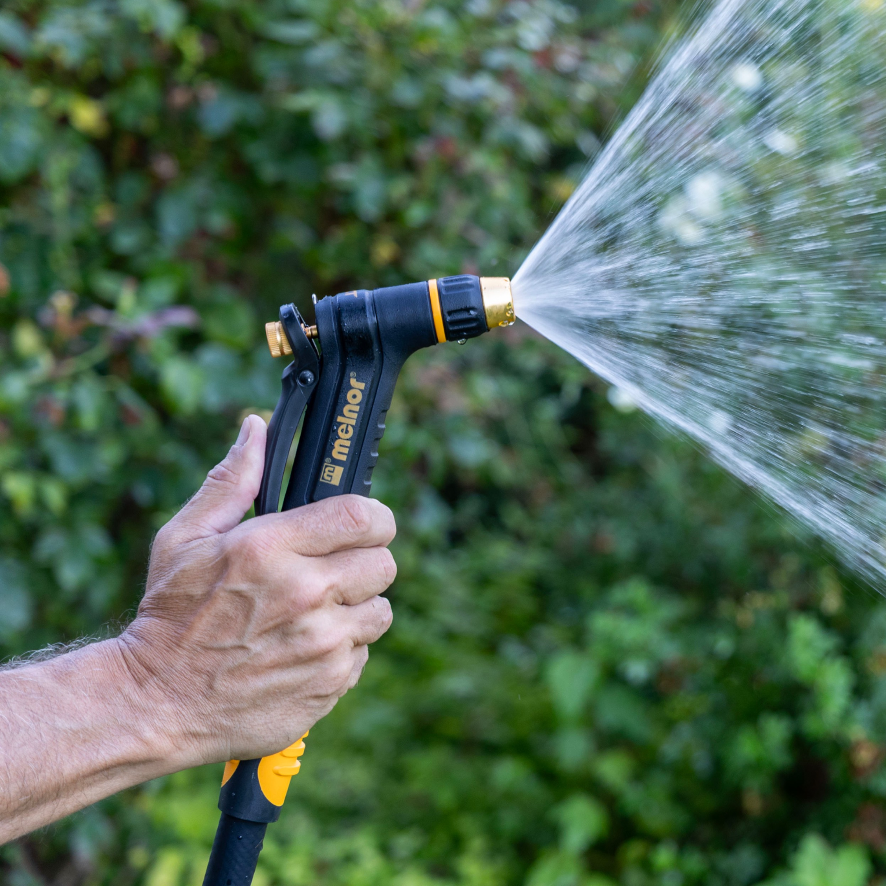 Melnor XT200 Rear-Trigger Adjustable Nozzle turned to the mist setting in front of a blurred garden background.