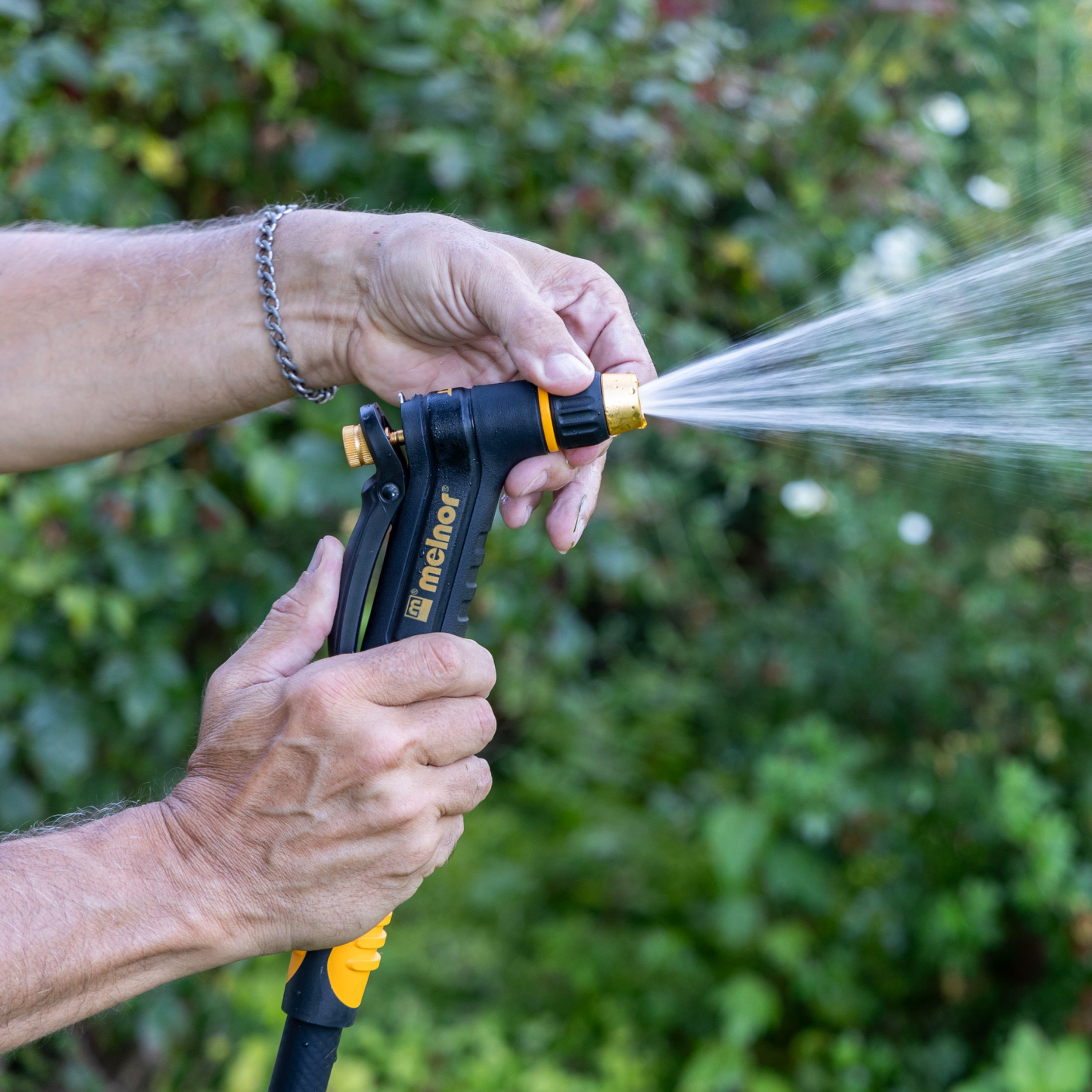 A hand using the twist function on the Melnor XT200 Rear-Trigger Adjustable Nozzle to change spray settings in front of a blurred garden background.