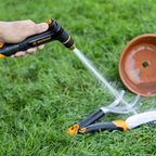 Melnor XT200 Rear Trigger Metal Adjustable Nozzle using the targeted jet spray setting on a gardening trowel and cultivator with a clay planting pot in the background on green grass.