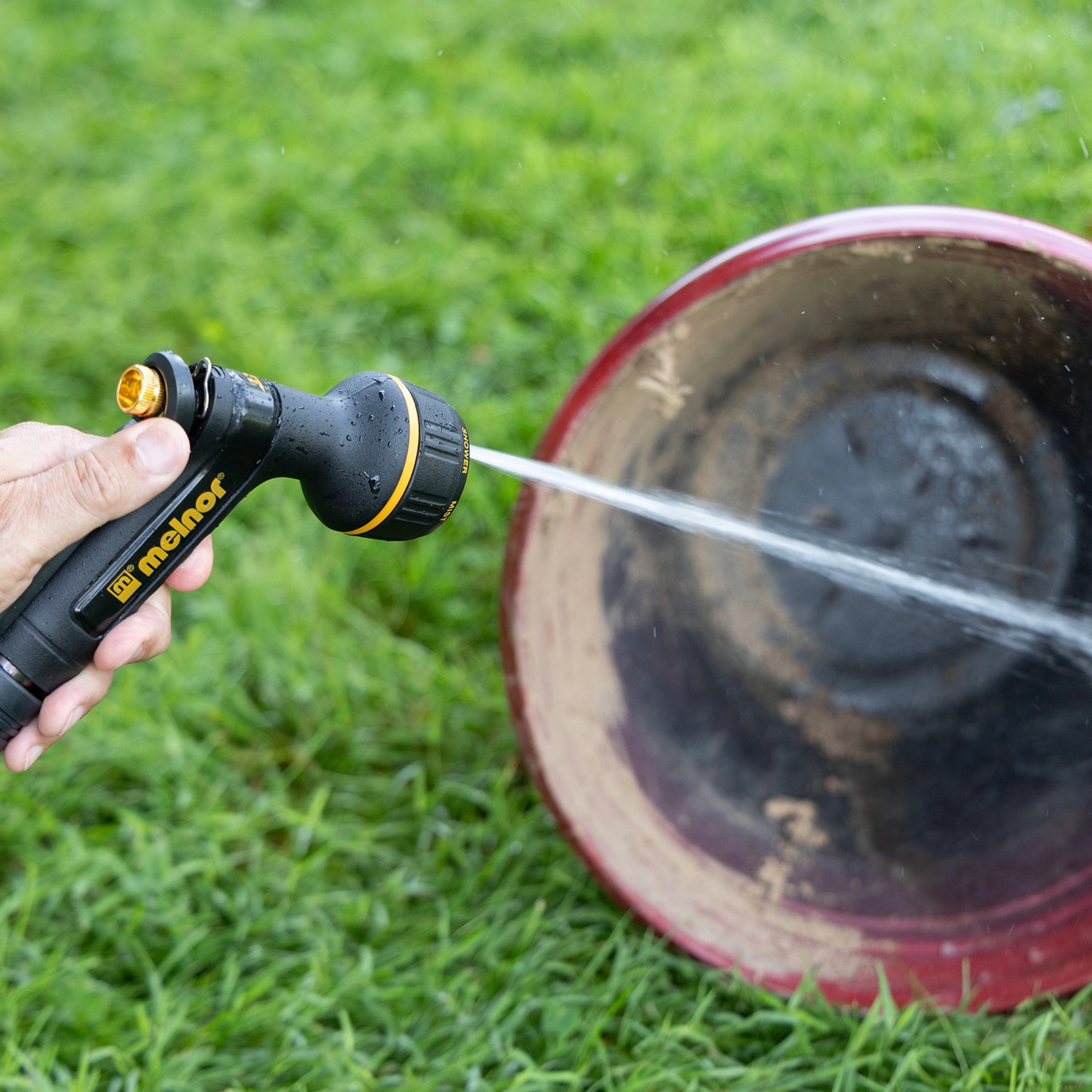 Melnor XT201 Rear Trigger Metal Seven Pattern Nozzle using the targeted jet spray setting on a large red plastic planting pot on green grass.