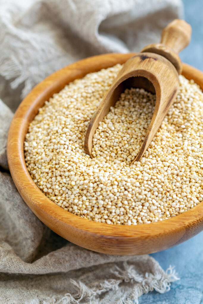 Uncooked quinoa seeds in a wooden bowl with a small scoop.